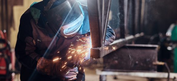 Man is working at metal factory, he is welding a piece of rail using special tools.