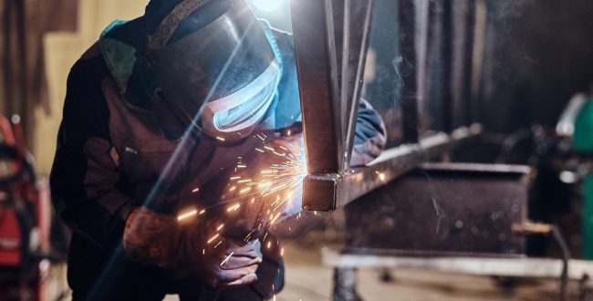 Man is working at metal factory, he is welding a piece of rail using special tools.